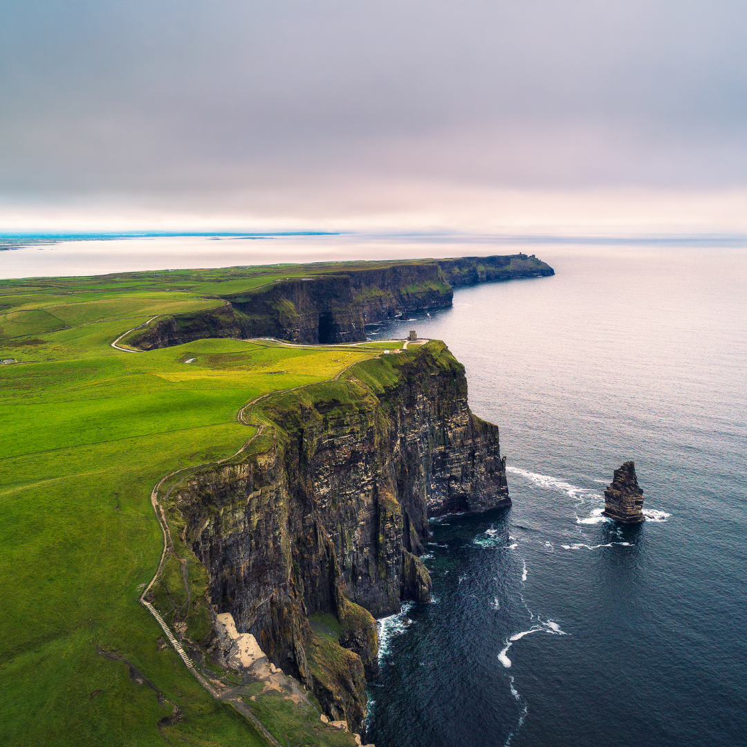 A panoramic view of Ireland’s lush green fields, rolling hills, and a historic stone castle beneath a dramatic cloudy sky.